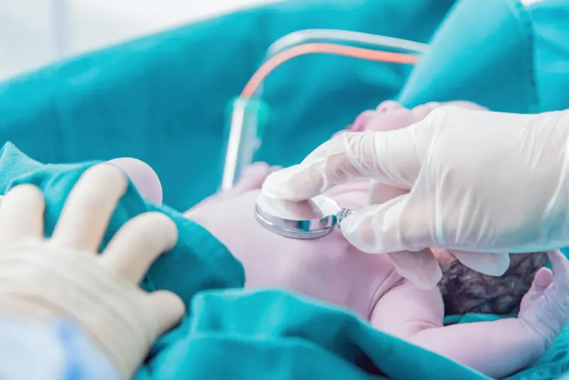 Çocuk doktoru yenidoğanı steteskopla muayene ediyor